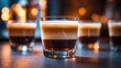 © Lasvu - Four glasses of layered coffee drink with dark and light sections, placed on a wooden surface with warm background lighting.