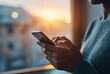 © dina - Cropped shot of hands holding a smartphone. Sunlight streams in behind. A woman is wearing a cozy gray sweater and looking down at the phone