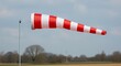 © Deki - Red and white striped windsock blowing in the wind indicating wind direction and speed against a