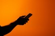© Loktor - Smartphone moderno con pantalla naranja brillante, Teléfono móvil en mano sobre fondo naranja, Fondo minimalista con smartphone encendido, Pantalla iluminada de móvil en contraste oscuro
