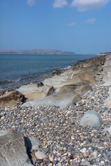 Wall Mural - Rocky coastline under a blue sky with distant hills.
