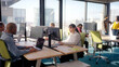 © CarlosBarquero - Group of colleagues working at computer stations in a bright modern office with city views, combining focus and collaboration while analyzing data and discussing tasks in a shared workspace.