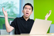 © fotolite - A young man gestures in frustration while staring at his laptop in a modern classroom. Showing technical issues, remote learning challenges, student stress, and teenage digital frustration.