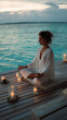 © Chris - Meditation Water Wellness: Elegant Woman Practicing Yoga at Sunset with Relaxing Candles on Wooden Deck in Coastal Nature for Inner Peace and Tranquility