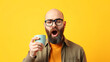 © Joshua - Concept of morning awakening and productivity. A bald, bearded man with glasses, holding a mug of coffee or tea and yawning lazily. Yellow background. Copy space