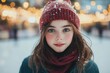 © hkjdesign - A girl with rosy cheeks, blue eyes, and a red knitted hat and scarf, stands in a snowy winter scene.