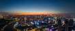 A wide view of a city at dusk shows bright lights and buildings.
