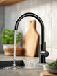 © Mr. Orsetto - Modern black kitchen faucet with running water over sink showcasing sleek design with blurred cutting board and fresh herbs in stylish contemporary home setting