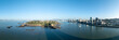 Coastal island panorama shows ocean and city skyline under a clear blue sky.