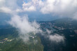 Jiugong Mountain in Xianning City China unfolds below a blanket of soft clouds, revealing a serene vista of lush green slopes and a tranquil lake surrounded by buildings.