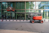 Red articulated boom lift parked on a city street in front of a modern glass building