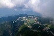 Jiugong Mountain Xianning China overlooks a serene lake surrounded by lush green mountains and scattered buildings under a partly cloudy sky.