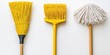 © Samady - Three cleaning tools â€“ a straw broom, a yellow push broom, and a coconut fiber mop â€“ are arranged side-by-side on a white surface.