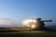 © Austockphoto - Harvester harvesting canola crop at dusk on farm