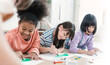© paulaphoto - Group of multicultural kids happily drawing with crayons on the floor during an art activity in a bright classroom setting. Education back to school