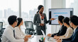 © stock for you - A woman in a suit leads a presentation to a diverse group in a modern office. They're engaged, analyzing data, with sunlight streaming through the window.