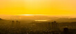 The sun shines brightly over the city skyline and a vast lake, casting a warm golden glow as it sets, creating a breathtaking panoramic view.