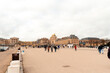 Visitors explore the grand entrance gate of Palatul Versailles, a historic site in France, as clouds loom overhead, creating a vibrant atmosphere of wonder and curiosity.