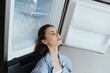 © SHOTPRIME STUDIO - Young woman enjoying fresh food and cool air from refrigerator, wearing casual denim jacket, reflecting healthy lifestyle and fresh food choices