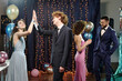 © AnnaStills - Group of teenagers celebrating prom night, girl and boy giving high five, boy and girl standing nearby, festive decorations and balloons in background