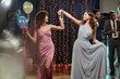 © AnnaStills - Teenage Caucasian girl dancing with young adult Caucasian woman at formal event, both smiling and holding hands, background showing people socializing and festive decorations