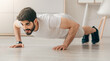 © Prostock-studio - Covid-19 pandemic and home workout for body care, online lesson of training during lockdown. Cheerful handsome arabian man with beard doing push-ups on floor in living room interior, free space