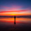 © simz - Solitary figure watches a vibrant sunset over the ocean reflecting on the wet sand