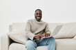 © SHOTPRIME STUDIO - Cheerful young Black man working on a laptop at home in casual knitwear, embodying comfort and productivity in a modern living space