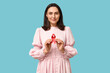 © Pixel-Shot - Pretty young woman holding red ribbon on blue background. World AIDS Day concept