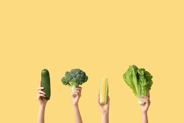 Wall Mural - Female hands holding fresh vegetables on yellow background