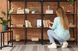 © Pixel-Shot - Young woman taking book from shelf in room, back view