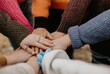 © Bumi - Close-up of many hands stacked together, symbolizing unity and teamwork; warm sweaters peek out, suggesting a supportive, collaborative atmosphere