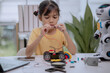 © FAMILY STOCK - Asian girl focused on building a robot car using wires, gears, and tools at home, concept of STEM education, robotics workshop, DIY engineering, and creative technology learning for kids.