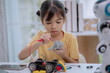 © FAMILY STOCK - Asian girl focused on connecting wires to robot motor at home, concept of STEM education, DIY robotics, maker space, hands-on engineering, and creative technology learning activities for children.