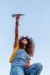 © Westend61 - Woman with curly hair playing with paper plane outdoors in public park