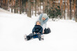 © Ljustina - Mother pushing son on sled in snowy forest during winter day