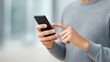 © Preeyanuch - Person using a smartphone, focused on the screen with a gray sweater in a bright environment.