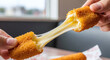 © izabella - A person pulling apart a mozzarella stick with cheese stretching between the two halves of the snack