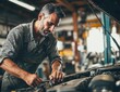 © ttonaorh - Close-up of a professional auto mechanic working on a car engine in a garage, wearing gloves and overalls, focused on repair.