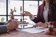 © Tj - Female lawyer explaining contract details to client during a meeting in the office, with scales of justice, gavel and digital tablet on wooden table