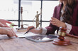 © Tj - Lawyer guiding client on where to sign a legal document, with scales of justice and a Themis statue prominently displayed in the background, creating a professional atmosphere