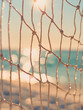 © ivlianna - Volleyball net moves gently in warm breeze near the tranquil shore during sunset with soft shimmering waves in the background