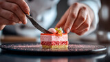 Chef decorating a layered pink dessert with a fork on a black plate close up