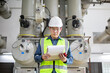 © JD Studio - Inspection substation worker wearing safety helmet and reflective vest holding clipboard and walkie talkie while checking equipment in industrial power substation environment