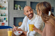 © we.bond.creations - Smiling couple eating healthy breakfast with orange juice and strawberries at home in the kitchen