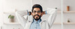 © Prostock-studio - Rest and relax during break, medical worker with gadgets. Smiling millennial arabian bearded doctor in white coat and glasses folded hands behind head at table with laptop in office interior, panorama