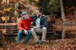 © Halfpoint - Son and older father sitting on bench by lake and talking.