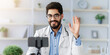 © Prostock-studio - Online consultation, remote visit to doctor and modern health care during covid-19 quarantine. Smiling young arabic medical worker in glasses and coat, waving hand to phone webcam, in office interior