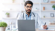 © Prostock-studio - Online medical support for patients during covid-19 quarantine. Attentive millennial handsome arabian bearded doctor in coat and glasses at table with laptop, makes notes in office interior in clinic