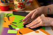 © Milan - Close-up of woman’s hands arranging black paper cutouts on bright colored sheets with Halloween designs.